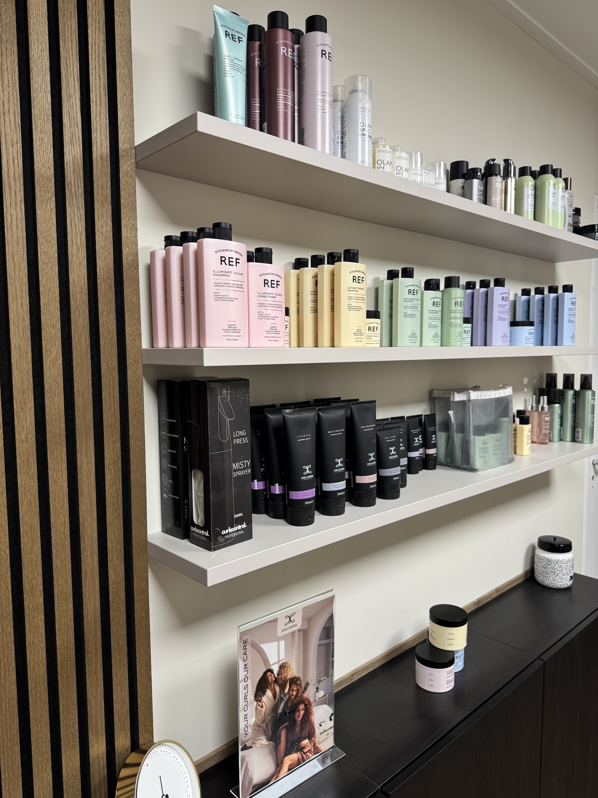 Wandplanken in de salon met shampoo, conditioner en stylingproducten naast de houten latjeswand